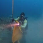 Scuba diver holding flare underwater near ocean floor