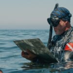 Snorkeler in wetsuit reading clipboard while standing in ocean
