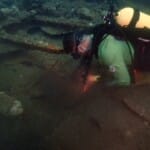 Scuba diver examining ancient underwater shipwreck remains on seafloor