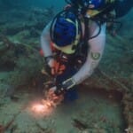 Scuba diver examining underwater shipwreck with camera equipment