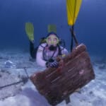 Scuba diver underwater holding an old wooden sign on sandy floor