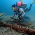 Scuba diver examining ancient shipwreck artifacts on ocean floor