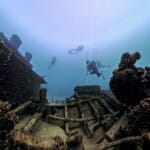 Scuba divers exploring a coral-encrusted underwater shipwreck