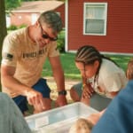 Adult and children examining contents of a clear container outdoors