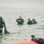Three scuba divers in wetsuits wading through open water