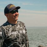 Smiling man wearing Force Blue shirt and cap by ocean