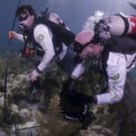 Two scuba divers exploring coral reef underwater with equipment