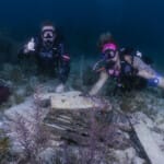 Two scuba divers exploring underwater wreck on ocean floor