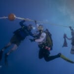 Three scuba divers holding a rope underwater in blue ocean