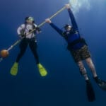 Two scuba divers holding a rope underwater in blue ocean