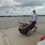 Man pushing cart with driftwood along waterfront dock