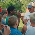 Adult coach giving instructions to group of kids outdoors